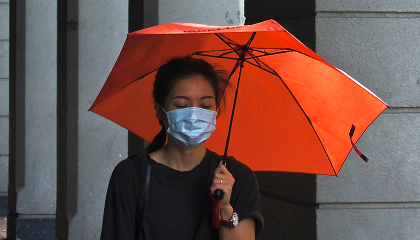 Woman holding orange umbrella, wearing a mask