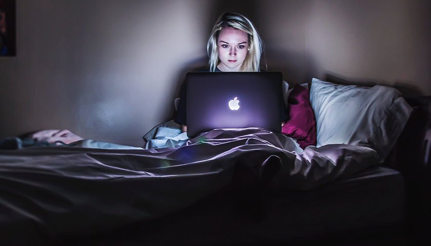 woman with blonde hair in bed on her laptop