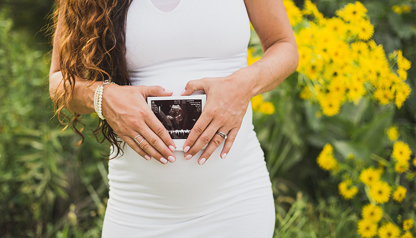 Pregnant woman holding ultrasound photo in front of stomach